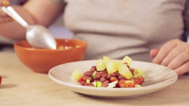 A woman's hand with a spoon puts the pineapple pieces into a plate of salad