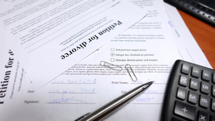 Blurred divorce contract papers with the husband signing it. Conceptual image for divorce with calculator and a hand signing the contract. Shallow depth of field with selective soft focus on the pen.