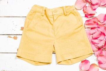 Yellow shorts on a white wood and some rose petals.The photograph is an overhead shot with a horizontal format.