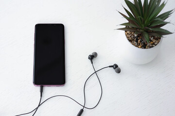 Smartphone with blank black screen and earphones on white table. Flat lay, mock up.