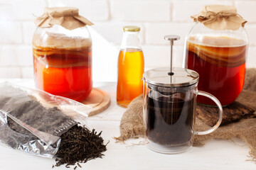 Set for preparing homemade fermeted drink. Glass jar with scoby, bottle with ready komucha and black tea brew. Light bricked background.