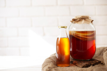 Glass jar with komucha scoby and bottle of ready beverage on light bricked background with copy space. Healthy fermented drink.