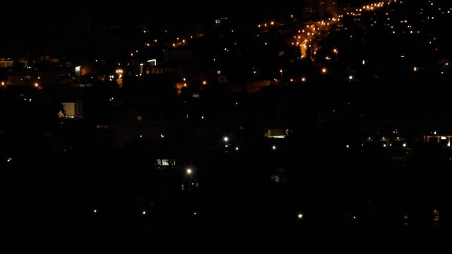 The lights of the city. Siluets leaves of trees swing in front of the camera. Night view from above