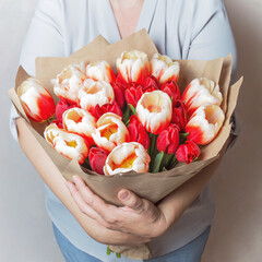 Bright red tulips wrapped in brown paper in female hands. A large bouquet of fresh cut spring flowers. A romantic gift for the holiday.