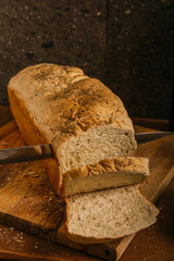 Homemade and artisanal loaf of fine herbs, a person with a knife slicing it on a wooden table.