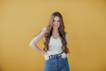 Portrait of a smiling blonde young woman standing isolated over yellow background