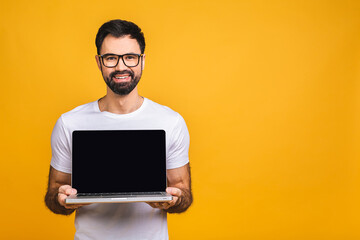 Smiling businessman pointing finger on blank laptop screen isolated over yellow background. Looking at camera.
