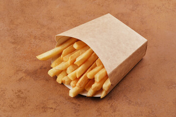 French fries in a brown kraft paper bag. Fast food. Food paper packaging from environmentally friendly materials. Eco friendly fast food containers. Brown background. View from above.