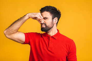 Caucasian bearded man isolated over yellow background smelling something stinky and disgusting,...
