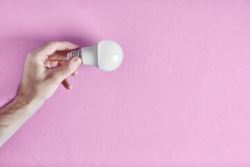 Young adult man's hand holding energy efficient light bulb against pink wall background. Concept of creativity, efficiency and sustainability.