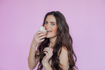 Portrait of a seductive young girl with bright makeup over violet background, eating cupcake