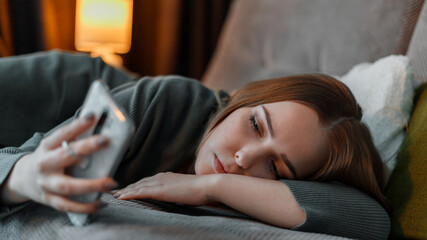 Sad teenage girl suffering from insomnia surfing Internet or chatting using smartphone at night lying on bed. Depression Internet addiction and depression in young woman. Long web banner - obrazy, fototapety, plakaty