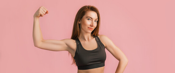 Fitness girl smiling in black sportswear on a pink background. Slim woman with a beautiful athletic body and tanned skin