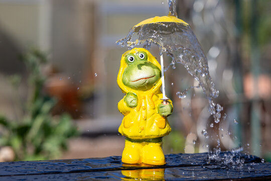 frog figure with rain jacket stands in the rain in spring and is protected by a yellow rain umbrella, symbolizing unusual weather in the season