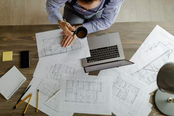 Architect sketching a construction project while he is drinking a coffee, view from the top.