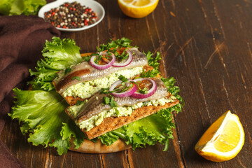 Fototapeta na wymiar Nutritious delicious breakfast, rye crisp bread with sardine fillet and cream cheese with herbs. Close-up, on a dark wooden background, a copy of the space