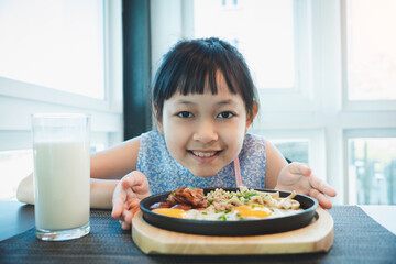 Asian little girl smiling with fried egg and fresh milk in breakfast
