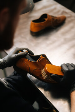 Close-up back view of unrecognizable shoemaker cleaning with brush old light brown leather shoe. Concept of cobbler artisan repairing and restoration work in shoe repair shop.