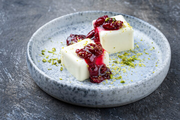 Modern style traditional blancmange almond pudding with sour cherry coulis and pistachios served as...