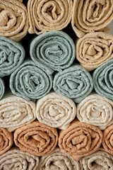 Home towels made of natural muslin in pastel shades are folded neatly in a row and decorated with a rope with a bead. Natural, soft and stylish home textiles. Grey background. View from above.