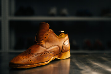 Close-up side view of old light brown leather shoes with wooden shoe pad to be repaired in dark craft shoe shop. Concept of cobbler artisan repairing and restoration work in shoe repair shop.