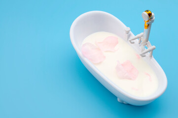 Skin pampering, cosmetic treatment and skincare therapy concept with bathtub filled with milk and pink rose petals isolated on blue background with copy space