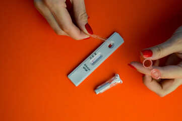 test for coronavirus on an orange background. a sensitive strip, a girl with a bright red manicure drips onto a drop of blood for a test and adds a physical solution there, a lancet lies nearby