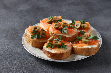 Canapes of salted salmon, green olives and parsley on croutons of white bread on dark gray background. Festive snack.