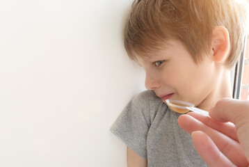 The boy turned away from the spoonful of medicine. Hand gives syrup on a spoon. The child does not want to drink, is dissatisfied, does not want to take medicine. Treatment of children at home.