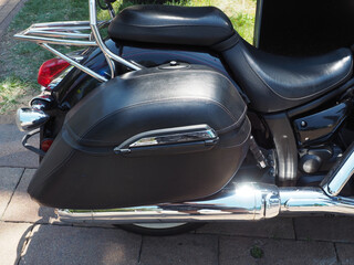 The back of a black motorcycle with a leather seat illuminated by sunlight