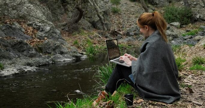 Freelancer woman working in laptop in the park near creek, remote job concept, fast 5g internet connection.