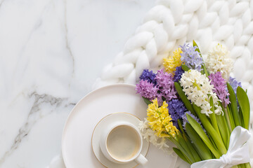 Top view composition with cup of coffee spring multicolored hyacinth on white fluffy knitted plaid