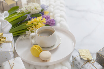 Top view composition with cup of coffee, pastry macarons and spring multicolored hyacinth on white fluffy knitted plaid