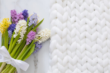 Bouquet of spring colored flowers of hyacinths. White marble background and fluffy knitted plaid
