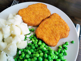 Breaded chicken escalope or chicken schnitzel with potatoes and green peas.  Golden crispy fried chicken. 