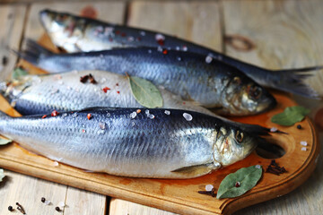 Salted herring of spicy salting. Spices and salt. Herrings with head and tail on a wooden board.