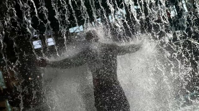 In The Water Park Behind The Waterfall There Is A Big Bald Man, Doused With Water, He Is In Swimming Trunks, A View From The Back.