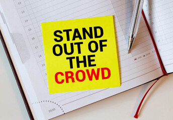 The words Stand out of the crowd written on a white notebook. Closeup of a personal agenda