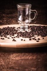 Empty cup of coffee with coffee beans around on a wooden board on a wooden table. Black background.