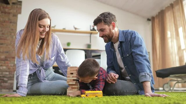 Happy couple of parents playing with little son on the living room floor. The fun-loving family enjoys spending their free time together on the weekends, building a building out of cubes