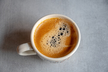 A cup of coffee in the morning light with an appetizing froth on a ceramic gray surface.