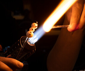 Hands of a glass artist, glass blower and their gas burner while making a decorative glass figure....