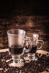 Cup of coffee with coffee beans around on a wooden board on a wooden table. Black background. Space for text.