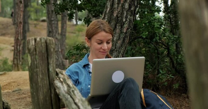 Freelancer woman using laptop in forest during hiking and traveling. Working remotely in nature. Fast 5g internet connection in forest.