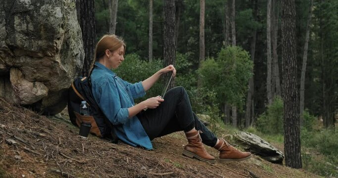 Freelancer woman using laptop in forest during hiking and traveling. Working remotely in nature.