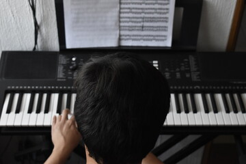 Joven tocando el piano teclado visto desde arriba con partituras