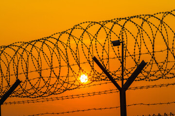 Silhouette of surveillance camera and barbed wire fence steel jail with the sunset in the background