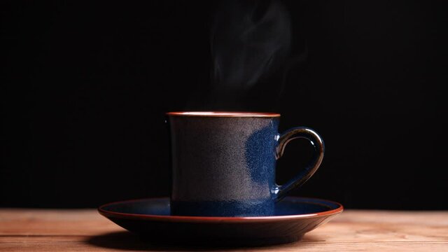 Coffee cup with natural steam smoke of coffee on wooden table, black background with copy space, slow motion. Hot Coffee Drink Concept.