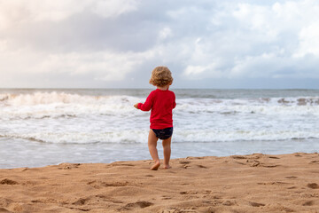 Fototapeta na wymiar Child walking towards the sea, on a beach in Guarapari, ES, Brazil.
