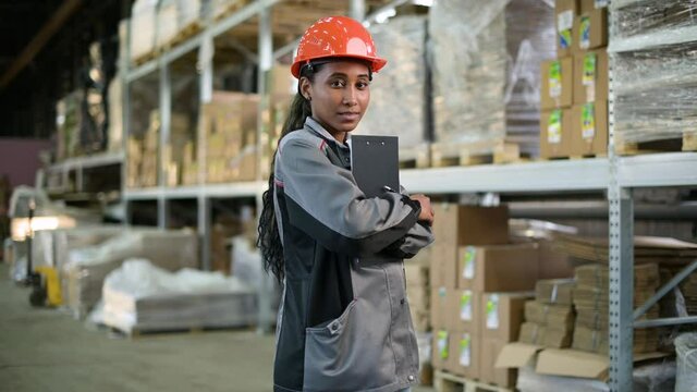 Portrait of a young black woman at work. Worker of production and warehouse in overalls and orange helmet